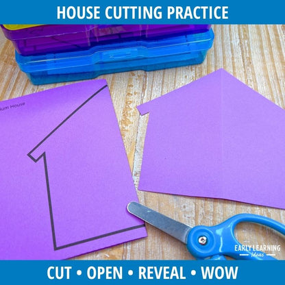 Purple fold-and-cut house template with number 1, blue scissors, and colored storage boxes on wood surface for scissor