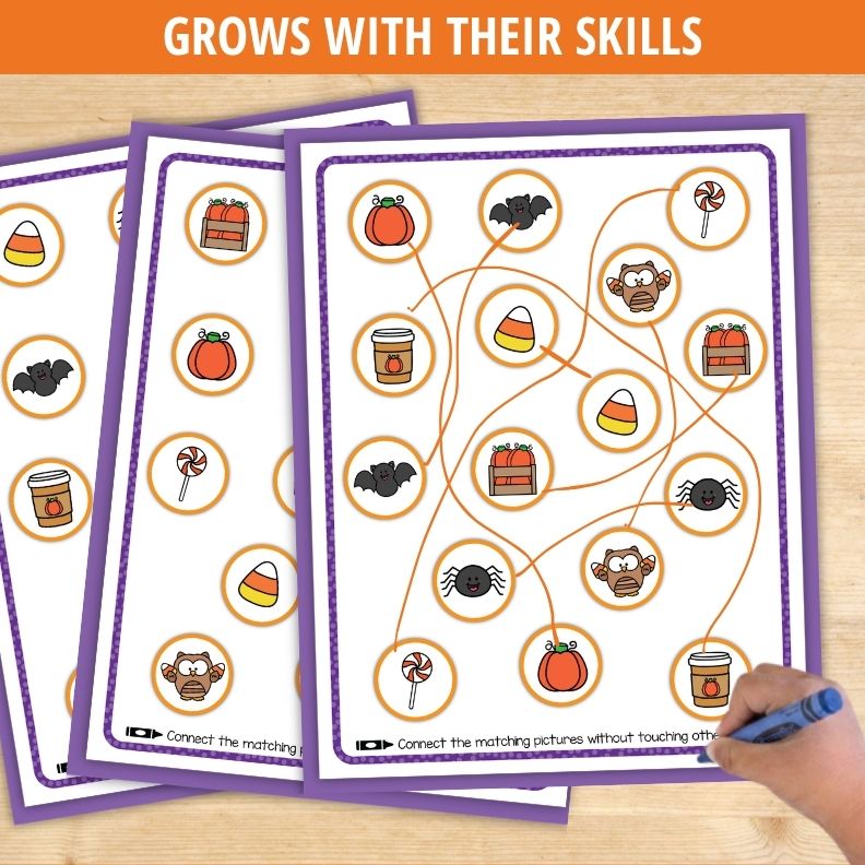 Child's hand drawing lines connecting Halloween pictures like pumpkins, bats, and candy corn in matching activity worksheet.