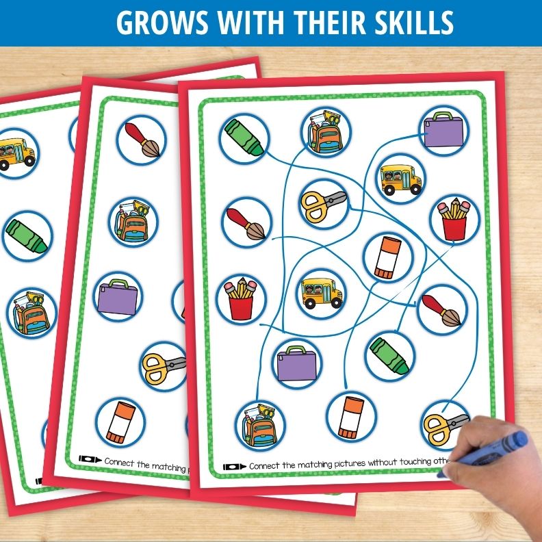 Child's hand drawing blue lines connecting school supply icons on laminated worksheet with red and green borders